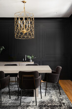 A Cozy Dining Room With A Gold Chandelier Above A Wooden Table And Black Wainscoting Walls.