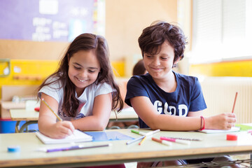 Two young caucasian children having fun doing homework together in class. Primary education. Back to school concept.