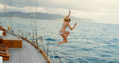 Poster - Carefree young woman in a bikini jumping from boat into the ocean. Woman on holiday jumping from a boat during a cruise to swim in the ocean. Woman sailing on a yacht jumping into the ocean to swim