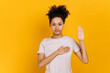 Only the truth. Honest proud curly-haired young african american woman in casual t-shirt, keeping hand on chest and raising palm, giving promise, oath, standing on isolated orange background