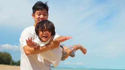 Happy family of dad carrying son flying play outside on the beach together having fun enjoy freedom on summer vacation people lifestyle activity on weekend concept.