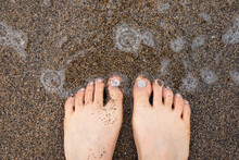 Wrinkled And Sandy Feet Of A Woman After Playing In The Water On A Sandy Beach Background.