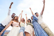 © JoseIMartin - Low angle view of a group of multi-ethnic friends raising their hands and laughing while posing together outdoors. Friendship concept.