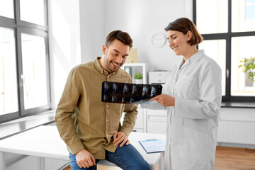 Canvas Print - medicine, healthcare and people concept - happy smiling female doctor showing x-ray to male patient at medical office in hospital