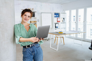 Young business woman standing with laptop in office
