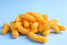 Heap Of Tasty Cheesy Corn Puffs On Light Blue Background, Closeup View
