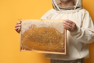 Wall Mural - Beekeeper in uniform holding hive frame with honeycomb on yellow background, closeup