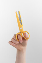 Child Hand Holding Yellow Scissors For Left-handers. White And Gray Background With Copy Space