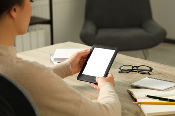 Canvas Print - Young woman using e-book reader at wooden table indoors, closeup