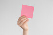 © Alexander - child hand holding a square pink blank reminder or paper notes above a white and gray background, copy space