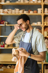 Aufkleber - Young tired black man with towel touching his head after hard work over creating new handmade clay items for sale in workshop