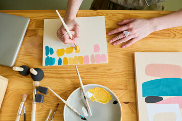 Aufkleber - Above view of hands of young creative woman making color swatches on paper while sitting by table and working over abstract painting