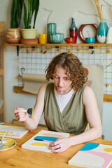 Aufkleber - Creative female sitting by table in studio or workshop and creating new abstract painting with help of sponge for applying paint on paper