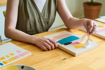 Aufkleber - Hands of young creative female sitting by wooden table in workshop or studio and using stencil while creating new abstract painting