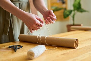 Aufkleber - Hands of young female clerk or artisan tying white cotton thread over roll of wrap paper by wooden table while preparing order of client