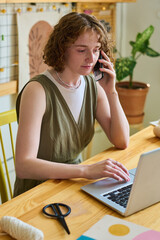 Aufkleber - Young serious woman with smartphone by ear talking to client while sitting by table in front of laptop and looking through online orders