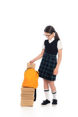 Wall Mural - Full length of preteen schoolgirl putting book in backpack on white background.