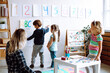 © Татьяна Волкова - Little girls and educator looking at boy showing pictures on wall in playroom. Interesting logic and intelligence lesson for kindergartners. Communication and development of mental abilities in kids