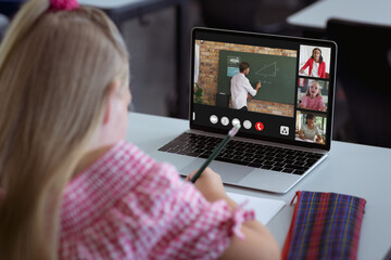 Wall Mural - Caucasian girl writing notes while looking at laptop screen during online class at home