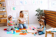 © Татьяна Волкова - Woman educator play with children sitting on floor in kindergarten. Kids folding blocks and drawing with colored pencils in playroom. Toys for kindergartners, development of thinking and intelligence