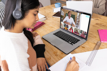 Wall Mural - Biracial girl writing while listening to teacher dictating notes on video call during online class