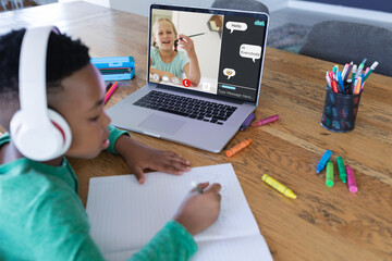 Poster - African american boy wearing headphones writing notes in book while attending online class on laptop