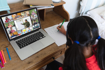 Wall Mural - Biracial girl writing english notes in book while attending online class over video call on laptop