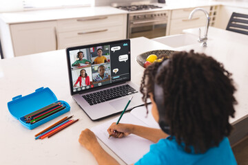 Poster - Biracial boy with colored pencils on table writing notes while studying online over laptop at home