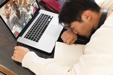 Canvas Print - Bored asian teenage boy sleeping in front of laptop during online lecture on table at home