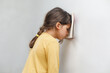 Sad and tired caucasian girl with dyslexia holds a wall. The child learns to speak and read correctly