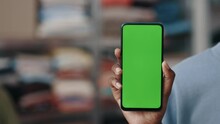 Multiracial Woman Holding Smartphone With Green Mock Up Screen And Showing It To The Camera While Standing At The Reuse Center. Cropped View