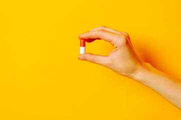 Female hand hold pill on yellow background