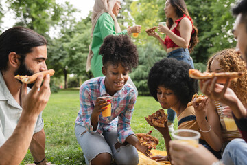 multiracial friends enjoying a party outdoors in the park while eating pizza