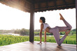 Concentrated fit girl stretching body muscles during morning pilates training near rice fields in Vietnam, flexible female yogi meditating for mindfulness keeping healthy lifestyle on retreat healing