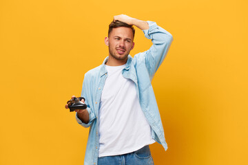 Wall Mural - Upset unhappy tanned handsome man in blue basic t-shirt lose game with joystick touch head posing isolated on orange yellow studio background. Copy space Banner Mockup. People lifestyle concept