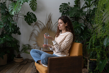 Wall Mural - Relaxed calm woman playing with spring toy for stress relief sit crossed legs in armchair. Female relieve stressful tension with stretchable spring has break from work at home office in indoor garden