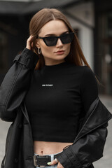 Wall Mural - Urban female portrait of beauty street fashion woman with cool vintage stylish sunglasses in black leather coat and black t-shirt walks on the street