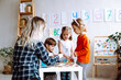 © Татьяна Волкова - Little kids with educator folding details of constructor on desk in playroom back view. Interesting game for kindergartners developing logic and intelligence. Communication with peers in kindergarten