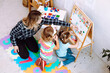 © Татьяна Волкова - Little kids and educator studying numbers and alphabet on magnetic board sitting on floor in playroom from above view. Interesting lesson for kindergartners developing logic and intelligence