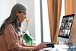 © Kateryna - Virtual meeting, online business meeting. Serious asian mature gray-haired woman communicate with business partners by video call uses app and computer, sitting at her work desk