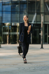 A female realtor in a blazer is walking with a laptop between skyscrapers.