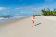 Woman In Bikini Walking On Beach Sand Against Blue Sky.