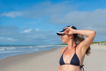 Portrait of woman in black bikini against beach and blue sky.