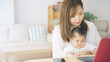 © metamorworks - 赤ちゃんを抱っこしながら自宅で仕事する女性　子育てしながらの在宅勤務