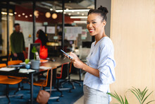 Portrait Of Smiling African American Businesswoman Using Smart Phone In Creative Office