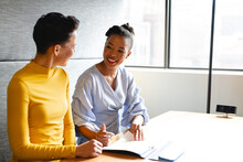 Smiling Multiracial Businesswomen Discussing Over Document In Creative Office