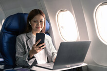 Happy And Cheerful Asian Businesswoman Using Smartphone And Laptop Computer During Flight. Urban Lifestyle
