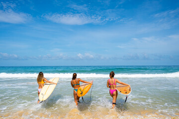  Group of Asian woman surfer in swimwear holding surfboard walking together on tropical beach in sunny day. Female friends enjoy outdoor activity lifestyle water sport surfing on summer vacation