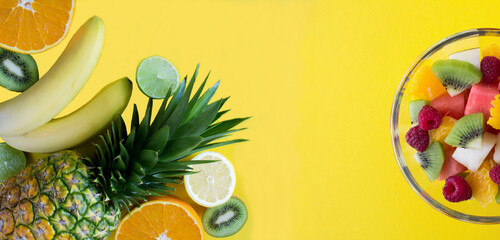 Wall Mural - Banner. Tropical fruits and fruit salad in the glass bowl on the yellow background. Close-up. Copy space.