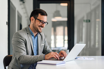 Wall Mural - smiling young entrepreneur typing on laptop while working at office desk